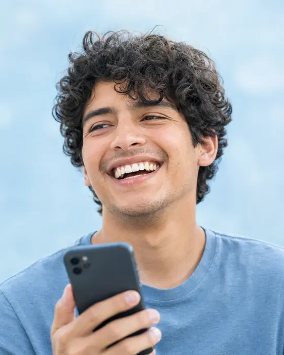 A young man laughing while holding his smartphone